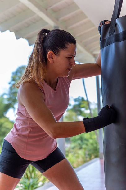 Young woman doing boxing training at home, she is wearing boxing gloves and hitting the punching bag - Fotoğraf, Görsel
