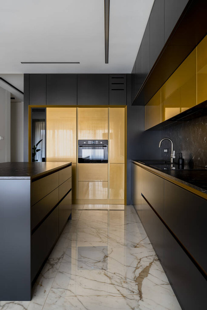 Елегантна кухня з чорно-золотими меблями, кухонним островом і мармуровою плиткою підлоги
 - Фото, зображення