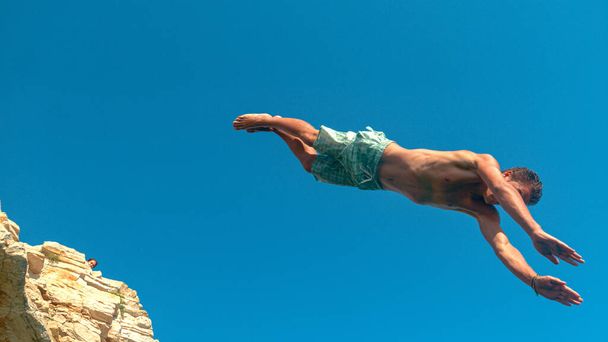 CLOSE UP: Спортивний турист стрибає зі скелі, щоб зануритися в освіжаючий океан
. - Фото, зображення