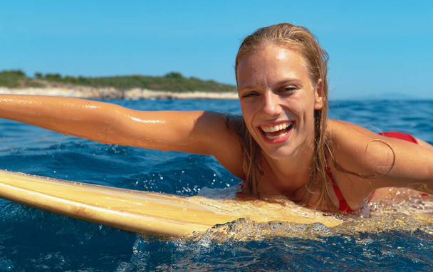 Vrolijke blanke vrouw liggend op haar surfplank zwemt naar de line-up. - Foto, afbeelding