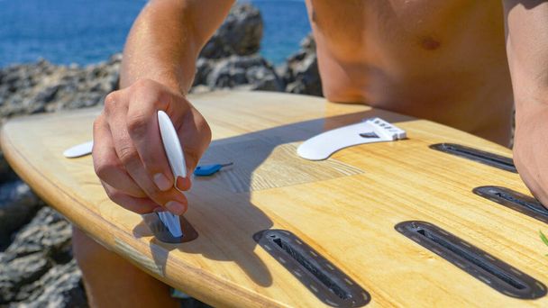 CERRAR: Surfista irreconocible sujetando aletas blancas en la parte inferior de su tabla de surf. - Foto, imagen