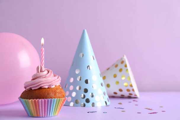 Delicious birthday cupcake with candle near party hats  and balloon on violet background, space for text - Photo, Image
