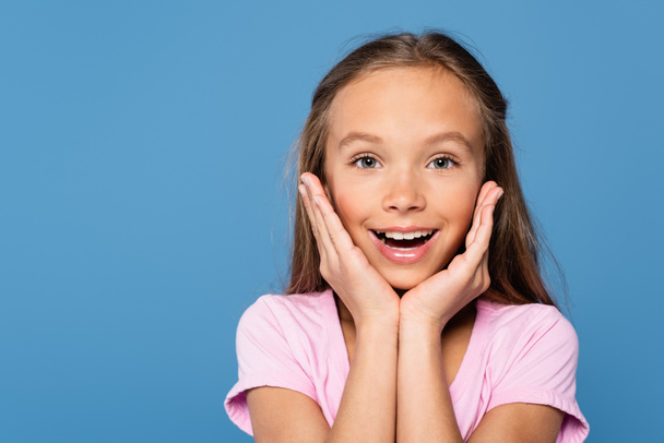 Smiling kid holding hands near face and looking at camera isolated on blue  - Foto, Imagem