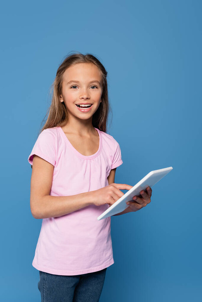 Girl with digital tablet smiling at camera isolated on blue  - Foto, imagen