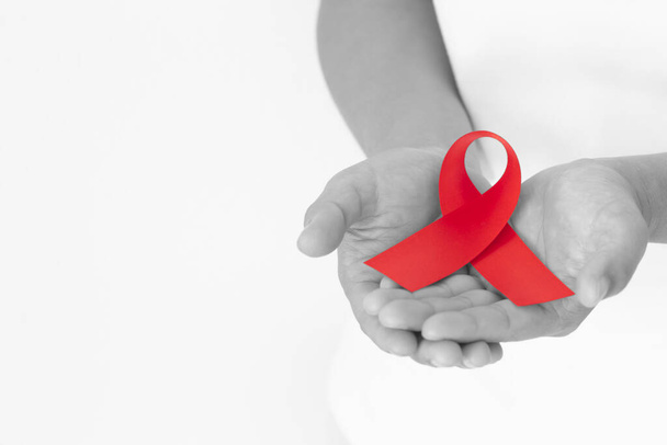 Hands holding red ribbon on white background copy space, symbol for the solidarity of people living with HIV/AIDS, and for the awareness and prevention of drug abuse and drunk driving. Health concept. - Photo, Image