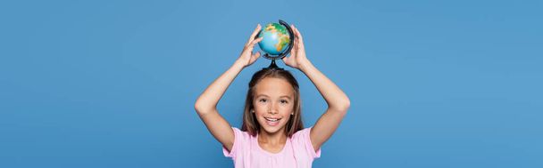 Smiling child holding globe above head isolated on blue, banner  - Foto, imagen