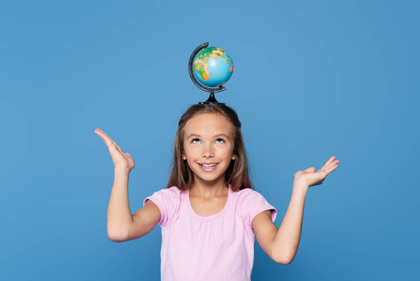 Glückliches Kind hält Globus auf dem Kopf isoliert auf blauem Grund - Foto, Bild