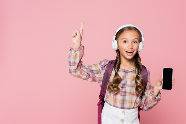 Positive schoolkid in headphones having idea while holding smartphone isolated on pink  - Fotoğraf, Görsel