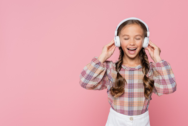 Happy kid listening music in headphones with closed eyes isolated on pink  - Photo, image