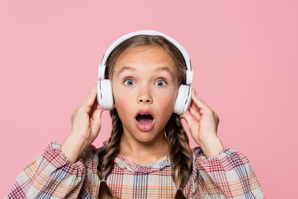 Criança incrível em fones de ouvido olhando para câmera isolada em rosa  - Foto, Imagem