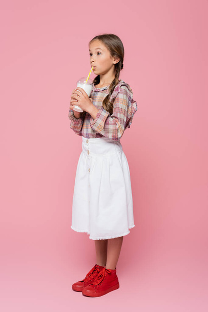 Stylish preteen girl drinking milkshake on pink background  - Photo, Image