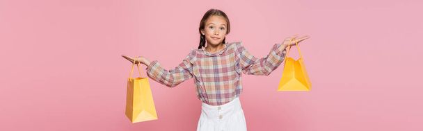 confused girl with yellow shopping bags showing shrug gesture isolated on pink, banner - Φωτογραφία, εικόνα