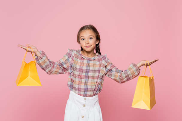 lány divatos ruhák mutató vonós gesztus, miközben gazdaság sárga bevásárló táskák elszigetelt rózsaszín - Fotó, kép
