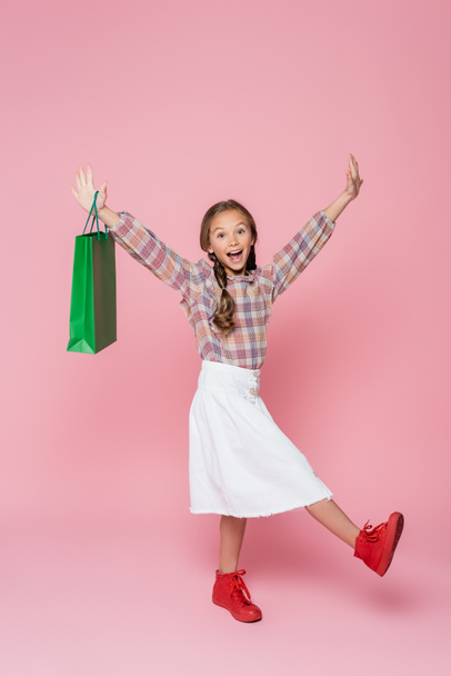 excited girl with green shopping bag raising hands on pink background - Foto, Imagem