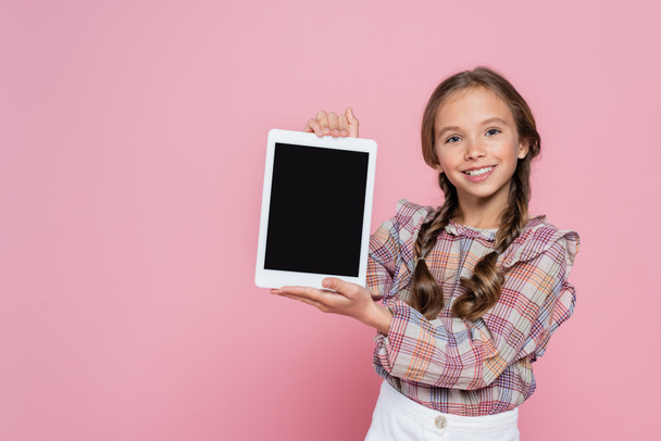 smiling girl in checkered blouse showing digital tablet with blank screen isolated on pink - Foto, imagen