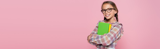 улыбающаяся девушка в клетчатой блузке и очках стоящих с книгами изолированы на розовый, баннер - Фото, изображение