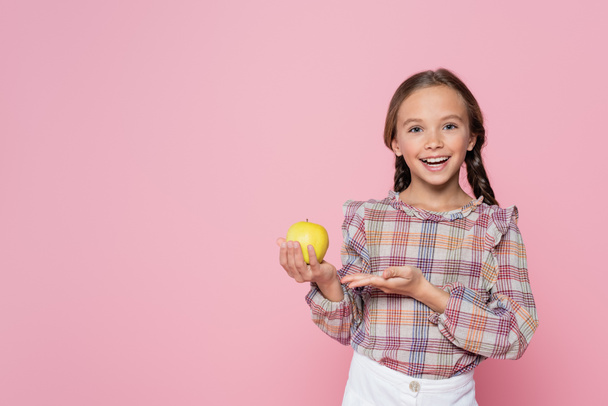 happy child in checkered blouse pointing at green apple isolated on pink - Photo, image