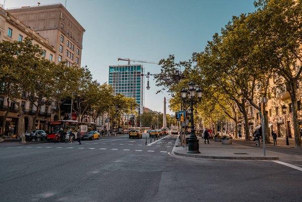 Barcelona, Spain - April 12, 2021 - street photography of an avenue with buildings, taxis, cars and obelisk in the background at sunset - Fotó, kép