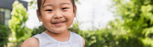 веселый азиатский ребенок смотрит в камеру снаружи, баннер - Фото, изображение