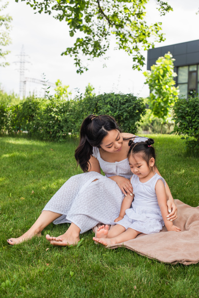 Aasialainen äiti katselee pikkulapsi tytär istuu piknik huopa  - Valokuva, kuva