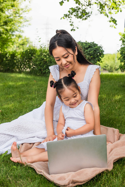 усміхнена азіатська мати і дочка дивиться фільм на ноутбуці в парку
  - Фото, зображення