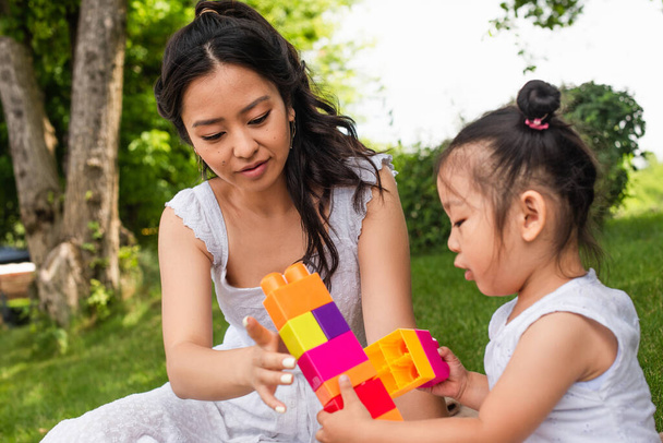 young asian mother and blurred toddler girl playing building blocks in park  - Photo, Image