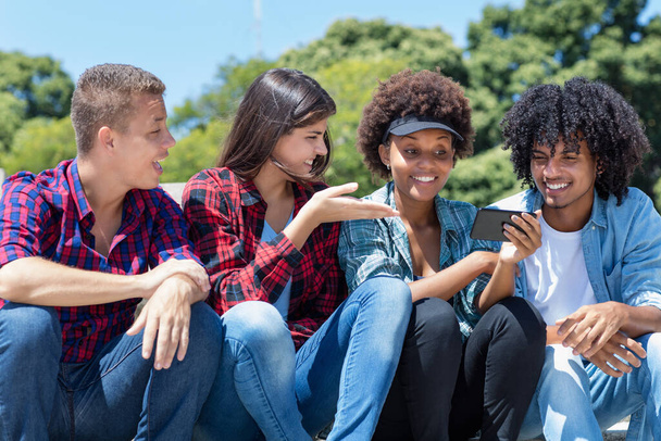 Group of latin and african american young adults watching clip on phone outdoor in city in summer - Photo, image