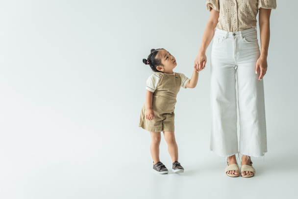 asian toddler kid holding hands with stylish mother on grey - Valokuva, kuva