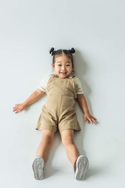 high angle view of happy asian toddler girl lying on grey - Foto, Imagen