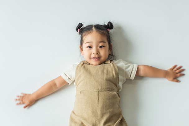 high angle view of happy asian toddler girl with outstretched hands on grey - Fotó, kép