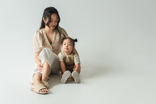 piena lunghezza di asiatico madre seduta con bambino figlia su grey - Foto, immagini