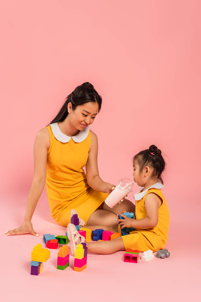 feliz asiático mujer y hija sentado y jugando bloques de construcción en rosa  - Foto, imagen