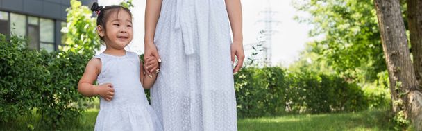 mother and toddler asian kid in dresses holding hands in park, banner - Photo, Image