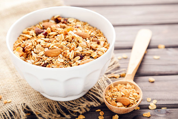 Tasty granola in bowl and spoon on brown wooden background - Zdjęcie, obraz