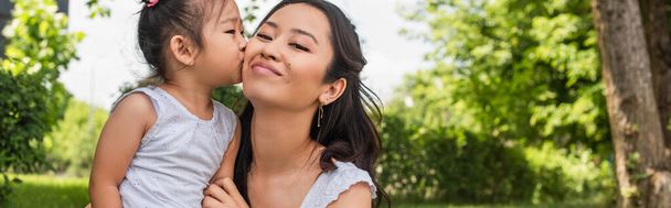 asian toddler girl kissing cheek of happy mother in park, banner - Photo, Image