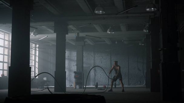 Hij vecht met touwen in de sportschool. Atletische man doet crossfit workout in loft gebouw - Foto, afbeelding