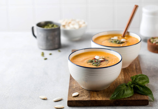 Two bowls of pumpkin cream soup on a wooden board, sprinkled with seeds. Autumn soup. Copy space. - Photo, image