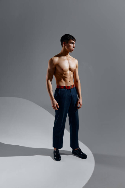 a handsome man with a naked torso in jeans and shoes stands on a gray background  - Фото, зображення