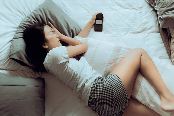 Exhaustion of woman fell sleep in bed in evening with smart phone in her hand. - 写真・画像