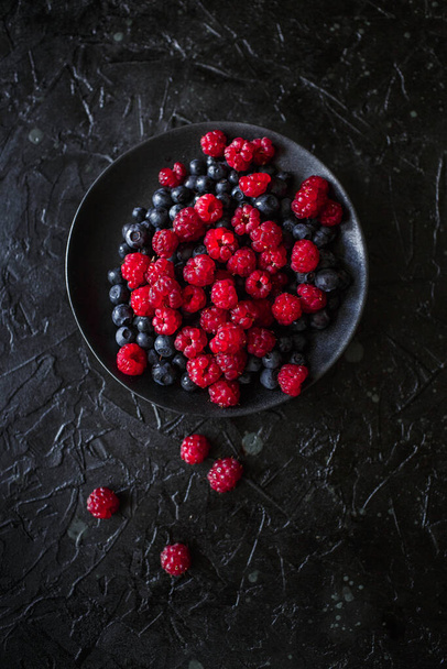 raspberries and blueberries, on a black background, wild berry - Photo, Image