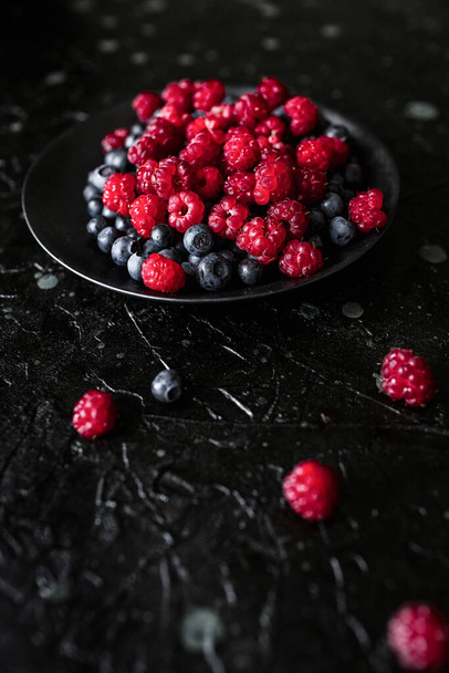raspberries and blueberries, on a black background, wild berry - Φωτογραφία, εικόνα