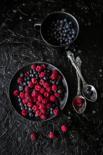 raspberries and blueberries, on a black background, wild berry - Valokuva, kuva