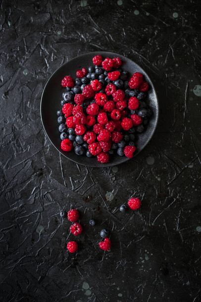 raspberries and blueberries, on a black background, wild berry - Photo, Image