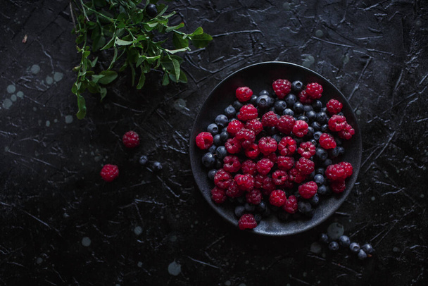 raspberries and blueberries, on a black background, wild berry - 写真・画像