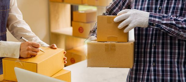 Young Asian woman starting a business and working happily with boxes at home preparing parcels in SME supply chain, omnichannel purchasing or online selling and delivery ideas. - Photo, Image