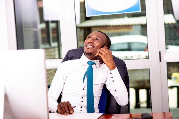 portret van een jonge zakenman praten op mobiele telefoon in het kantoor terwijl glimlachen. - Foto, afbeelding