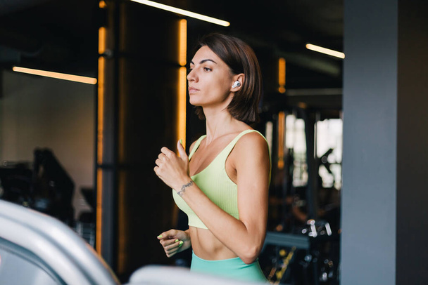 Fitt kaukázusi gyönyörű nő illeszkedő sport viselet edzőteremben futás futópad futópad a futópad vezeték nélküli fejhallgató fülébe - Fotó, kép
