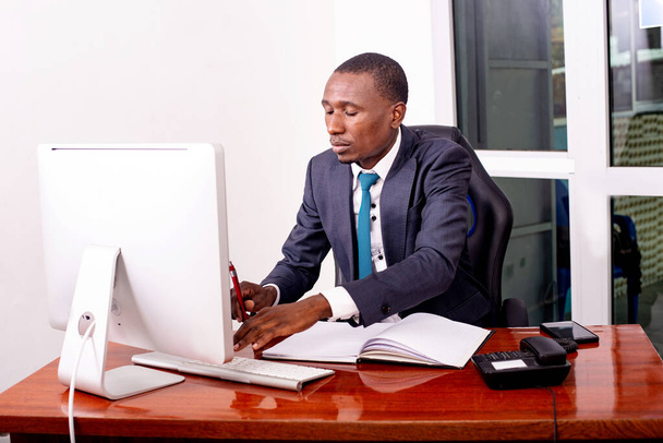 Poważny biznesmen pracujący na laptopie w biurze z dokumentem na stole. - Zdjęcie, obraz