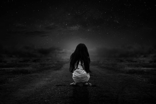 Een zwart-wit foto van een verdwaald meisje zittend in de eenzame avond - Foto, afbeelding