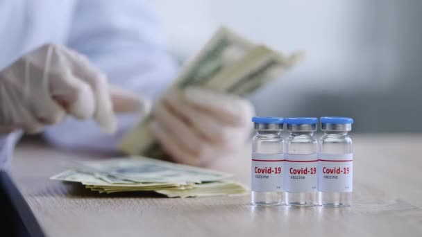 Coronavirus aşısı olan üç şişe kapalı kutu Covid için ilaç masaların üzerinde duruyor lateks eldivenli kadın eczacının elleri para tutuyor nakit para biriktiriyor - Video, Çekim